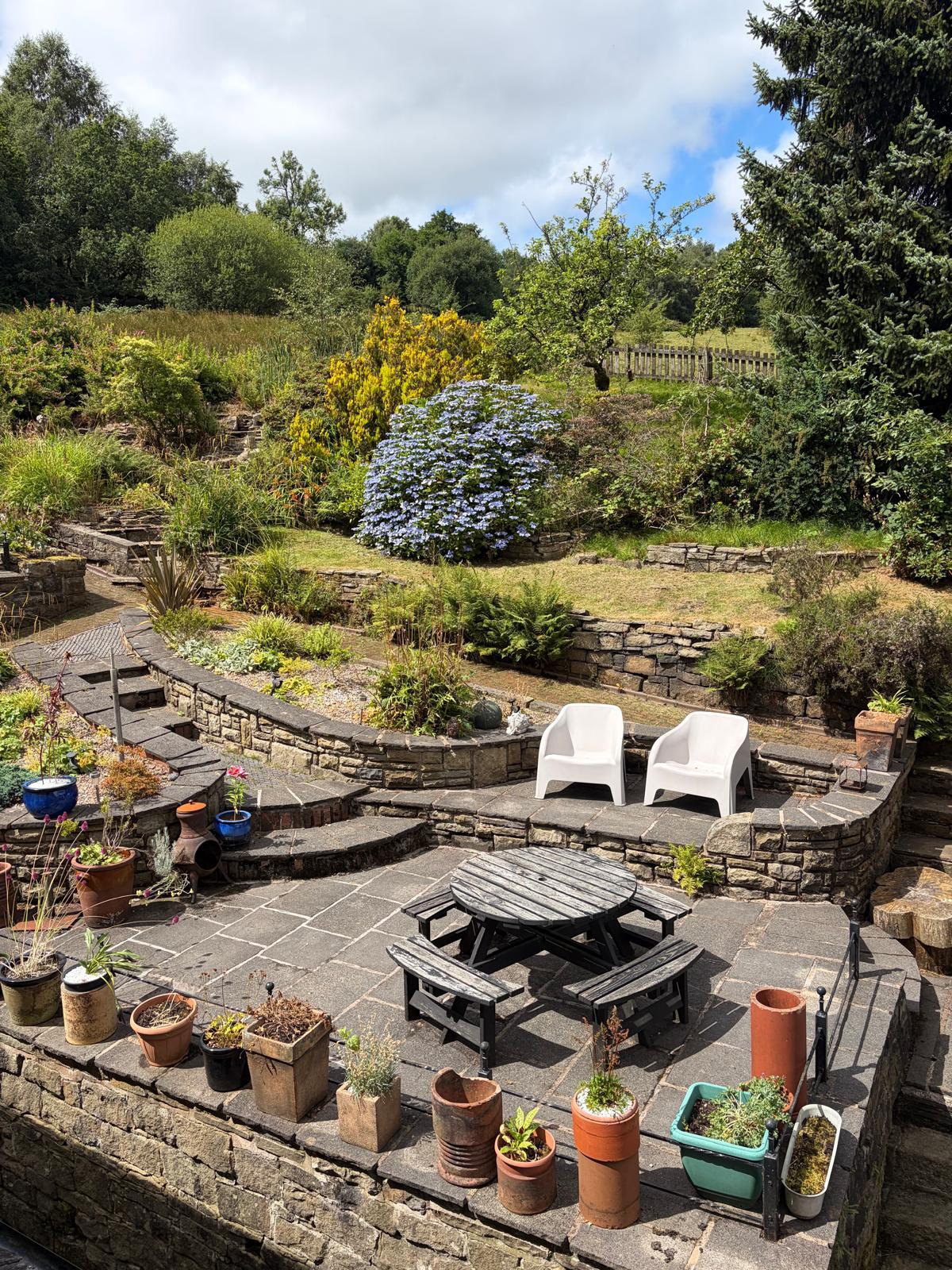 Terraced stone patio with a picnic table and potted plants above the valley