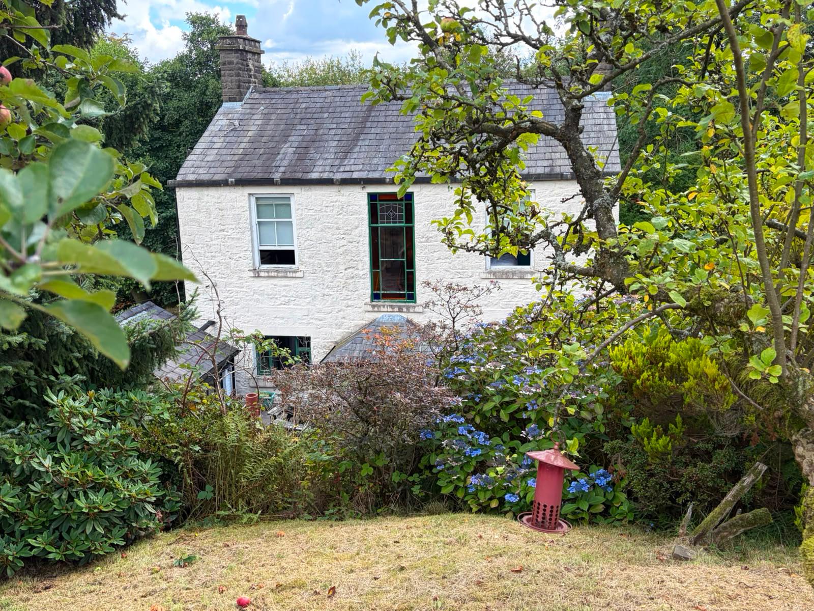 Rear of the cottage with stained glass window framed by an apple tree